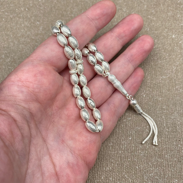 A rosary made of natural camel bone adorned with synthetic coral, featuring 33 beads and a silver cross with distinctive silver separators, crafted with a unique design